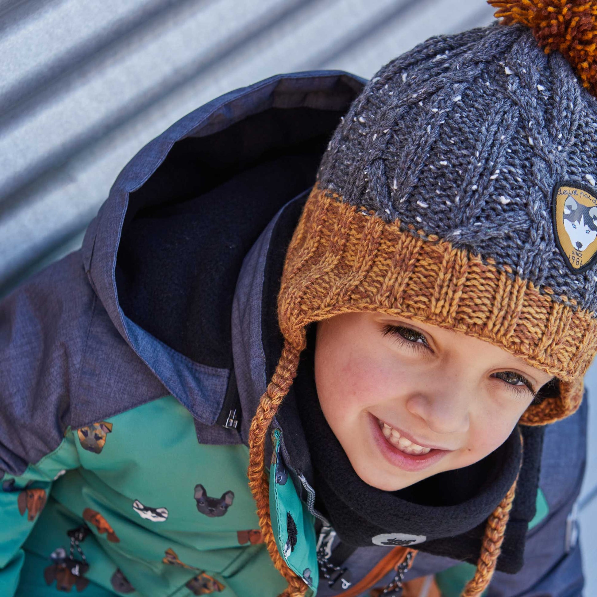 Marled yarn with contrast flecks adds contemporary style to our Earflap Knit Hat Grey and Yellow.  This winter hat is made from an acrylic/poly/wool blend and features braided tassel ties, rib knit trim, a logo patch, and a fluffy pompom on top.