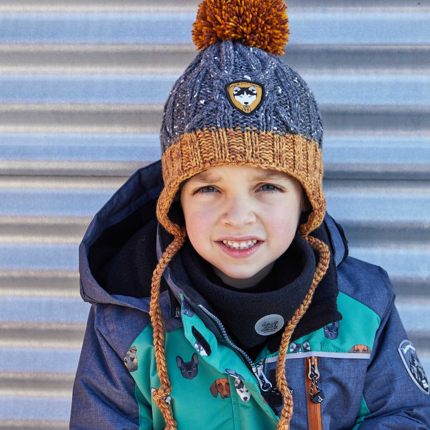 Marled yarn with contrast flecks adds contemporary style to our Earflap Knit Hat Grey and Yellow.  This winter hat is made from an acrylic/poly/wool blend and features braided tassel ties, rib knit trim, a logo patch, and a fluffy pompom on top.