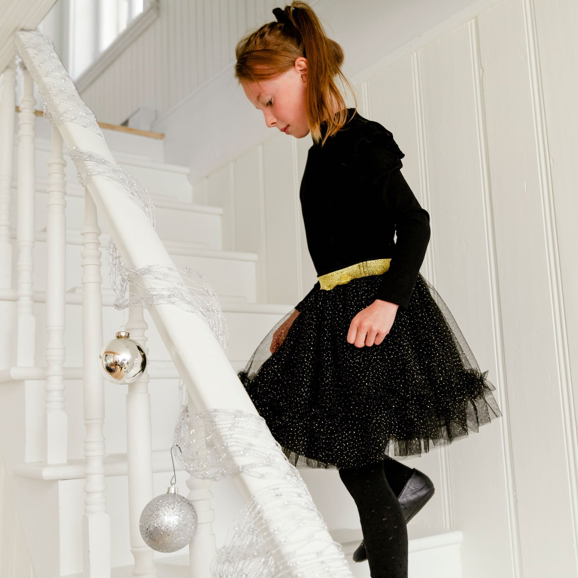 Our Gold Sparkle Dress With Black Frill is perfect for any little fashionista in the making.  This adorable party dress features a solid cotton bodice with long sleeves, ruffled shoulders, and a high neckline. The flared mesh skirt boasts a metallic elastic waistband, an allover glitter print, and ruffles near the hem.