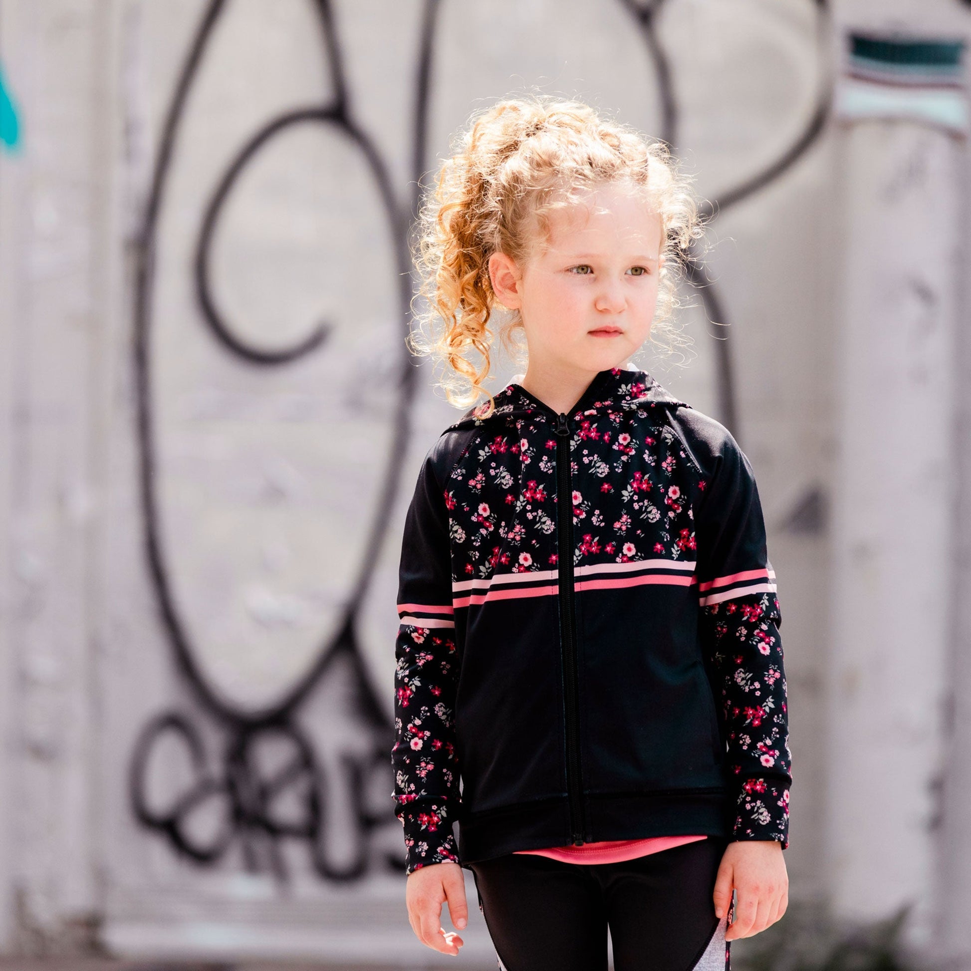 With floral print panels, this zip front jacket is equal parts sporty and sweet. Our Hooded Athletic Vest With Printed Flowers is made from stretch poly/elastane.  Features half-printed raglan sleeves, a printed hood, horizontal stripes across the chest and sleeves, and a logo print on the left chest.