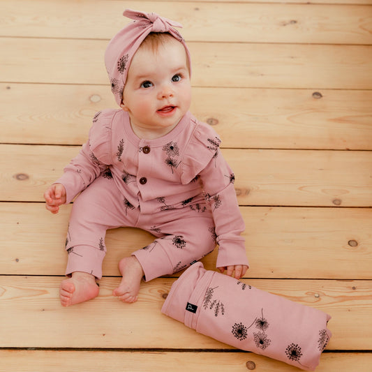 The Organic Cotton Hat and Bib Set Printed Flowers Dusty Purple features a soft hat with a bow on the front and a triangular bib with ruffle trim.